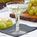 A Fineline clear plastic champagne glass filled with champagne and next to grapes.