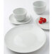 A Tuxton bright white coupe china plate on a white surface with cherry tomatoes.