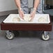 A person using a Cambro pizza dough box dollie to hold a tray of dough.