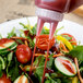 A hand pouring sauce onto a salad with vegetables using a Vollrath Traex clear bottle cap.