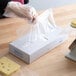 A person in gloves using LK Packaging plastic deli wrap on a table to cut cheese.