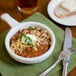 A Tuxton French casserole bowl filled with chili, cheese, and scallions.
