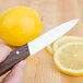 A hand holding a Victorinox paring knife with a small rosewood handle next to a lemon slice.