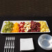 An American Metalcraft trapezoid melamine serving platter with fruit and forks on a table.