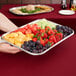 A person holding a Vollrath stainless steel tray of fruit on a table.