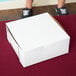 A person holding a 6" x 6" x 2 1/2" white bakery box.