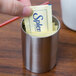 A hand placing a Splenda packet in an American Metalcraft stainless steel sugar packet holder.