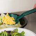 A hand holding a green Thunder Group salad bar spoon over a bowl of shredded cheese.