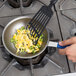 A person using a spatula to cook eggs and peppers in a Vollrath Wear-Ever non-stick fry pan with a blue handle.