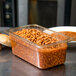 A Carlisle amber plastic food pan filled with baked beans on a counter.