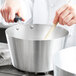 A person stirring a silver Vollrath sauce pan with a wooden spoon.