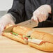 A person in gloves cutting a sandwich with a Mercer Culinary Millennia chef knife.