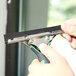 A person using a black and green Unger ErgoTec squeegee to clean a window.