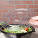 A hand holding a clear plastic lid over a Fineline clear plastic salad bowl.