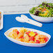 A Fineline white plastic luau bowl filled with fruit salad on a blue background.