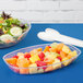 A clear plastic Luau bowl filled with fruit salad on a blue surface.