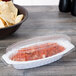 A Fineline clear plastic boat with salsa in it next to a bowl of chips.