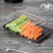 A Fineline clear plastic snack tray dome lid on a plastic container with vegetables.