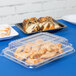 A Fineline clear plastic dome lid on a plastic serving tray with food inside.
