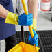 A person wearing blue Cordova dishwashing gloves with yellow lining holding a yellow mop handle.