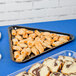A Fineline black plastic triangular tray with pastries on a blue surface.