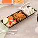 A Fineline black plastic sectional tiny tray with food on a table.