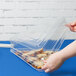 A hand placing food in a Fineline clear plastic triangular tray with a dome lid.
