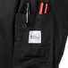 A pocket of a black Mercer Culinary Genesis chef jacket with a pen and a pen holder.