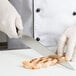 A gloved hand uses a Mercer Culinary MX3 Sujihiki Knife to cut meat.