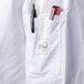 A white Mercer Culinary long sleeve chef jacket with a black pen in the sleeve pocket and a pen in the pen holder.