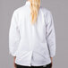 A woman wearing a white Mercer Culinary chef jacket with long sleeves and cloth knot buttons.