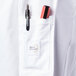 A close-up of the pocket on a white Mercer Culinary long sleeve chef jacket with a pen and a marker inside.
