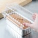 A hand holding a clear plastic container with a Durable Packaging foil bread loaf pan inside.