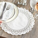A hand holding a plate with silverware on a white Normandy lace doily.