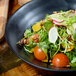 A bowl of salad with tomatoes and vegetables served on a black 10 Strawberry Street RPPLE stoneware plate.