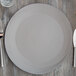 A 10 Strawberry Street matte gray stoneware charger plate with a knife and fork on a wooden table.