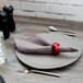 A 10 Strawberry Street gray stoneware charger plate on a table with a napkin and silverware.