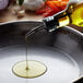 A person pouring Pure Olive Oil into a pan on a counter.