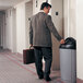 A man in a suit holding a briefcase and using a Rubbermaid Untouchable half round trash can lid with swing door.