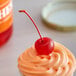 A frosted cupcake with an orange Maraschino cherry on top.