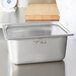 A silver Vollrath Super Pan with a clear lid on a counter.