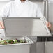 A chef using a Vollrath stainless steel pan cover on a tray of salad.