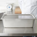 A Vollrath stainless steel pan cover on a metal container on a counter.