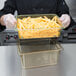 A person in a chef's uniform holding a Cambro amber plastic colander pan full of french fries.