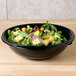 A bowl of salad in a Sabert black bowl on a table.
