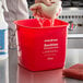 A person's hand washing a red sponge in a red Noble Products sanitizing pail on a counter.