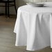 A table with a white Intedge 100% Polyester tablecloth and white plates on it.