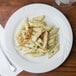 A close up of Tuxton Sonoma bright white china plate with pasta, chicken, and pesto sauce.
