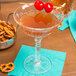 A Nachtmann cocktail glass with a drink and cherries on a table with pretzels.