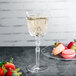 A Nachtmann white wine glass filled with wine next to a plate of strawberries and macaroons.